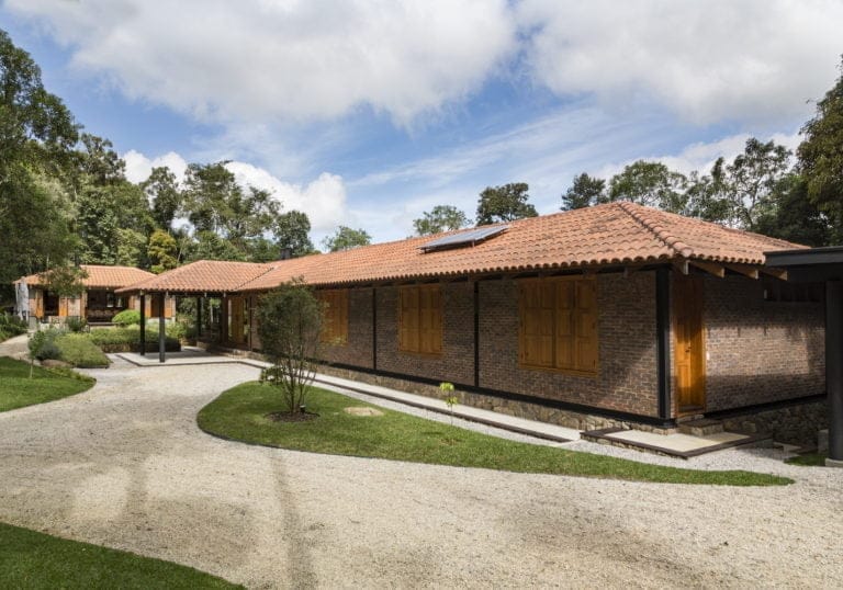 Long single-storey brick facade with terracotta roof and dark window frames beside gravel