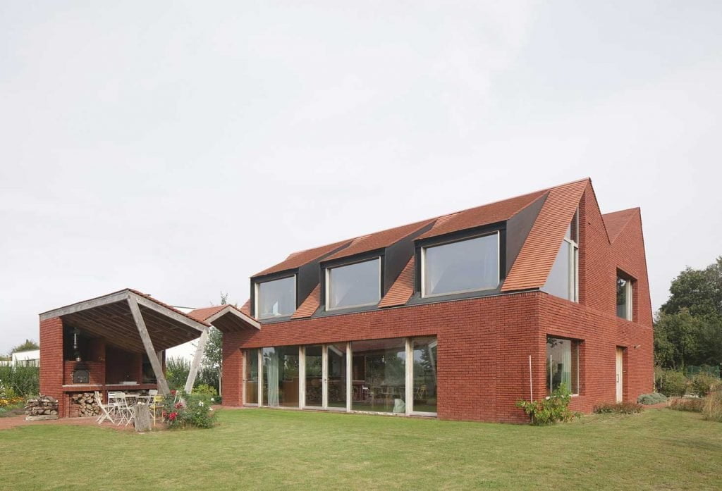 Facade of a two-story brick house with a roof stylized as brickwork