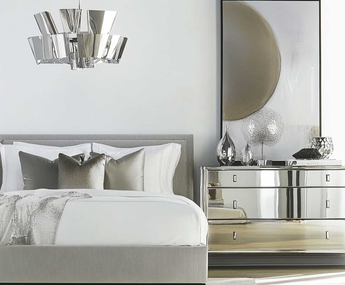 A sophisticated modern bedroom featuring unique silver lighting fixtures, including a sleek pendant light above the bed and minimalist wall sconces. The room has a plush gray upholstered bed with silver accents and crisp white linens. A mirrored dresser with silver handles stands opposite the bed, reflecting light and adding to the room’s luxurious feel. The walls are painted in a soft gray, creating a serene backdrop for the silver and white decor. The overall design is elegant and modern, with a focus on sleek lines and reflective surfaces.