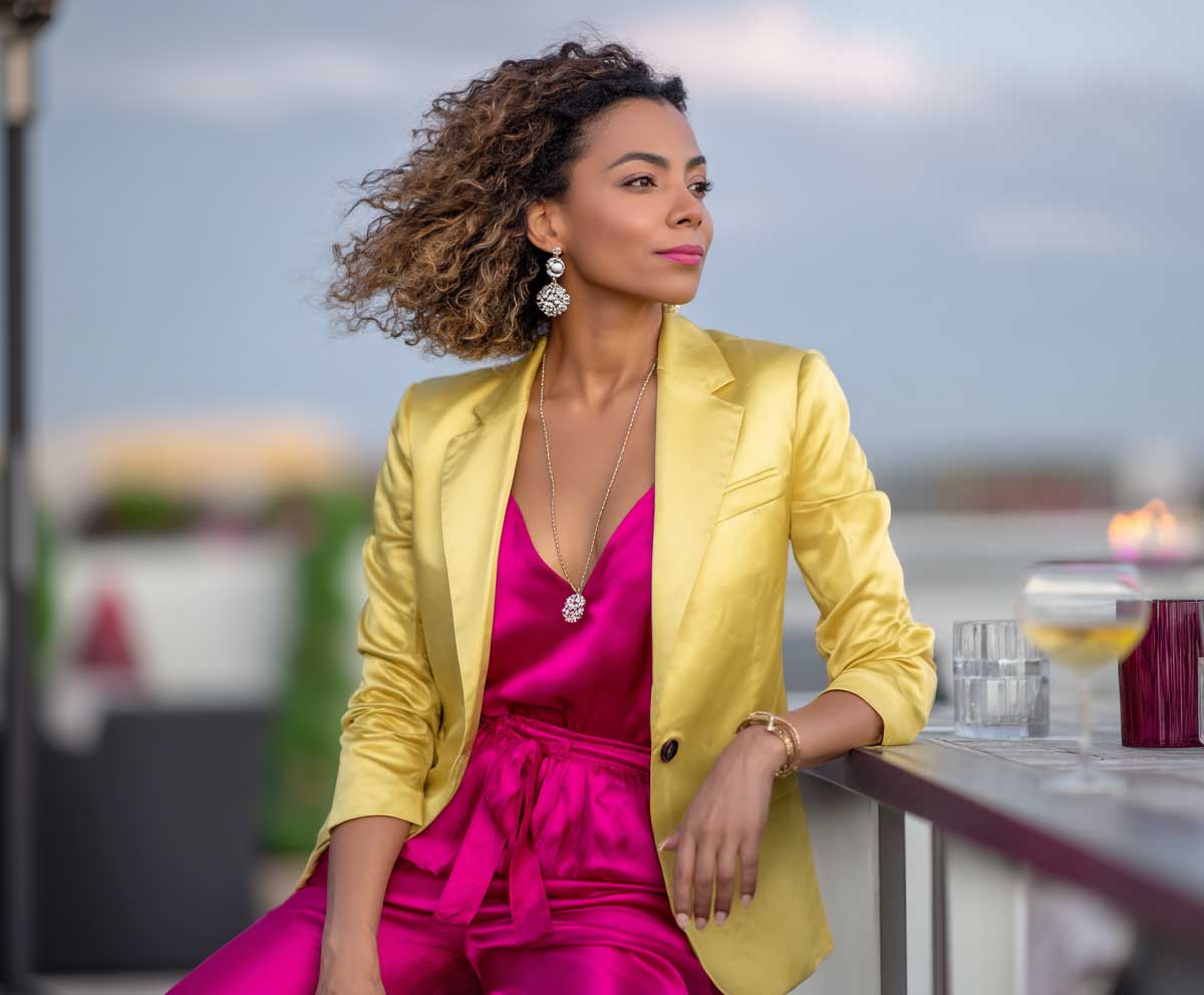 confident woman in a canary yellow blazer layered over a hot pink satin jumpsuit, rooftop restaurant setting, sunset sky, soft wind in hair, chic and vibrant style, natural makeup look