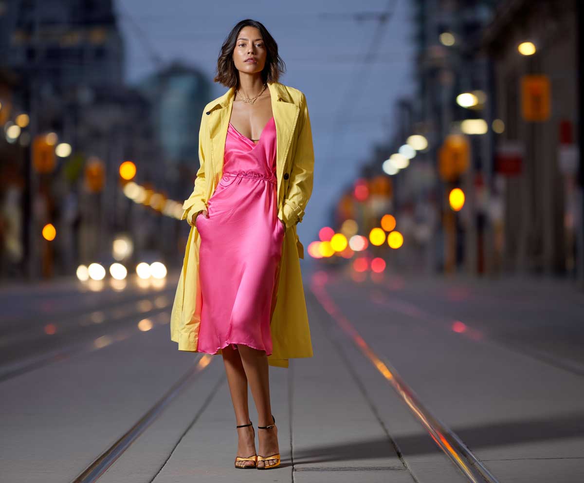 stylish woman wearing a silky hot pink slip dress layered with a canary yellow trench coat, city street at twilight, high heels, glowing streetlights, romantic urban atmosphere, full-body editorial photo