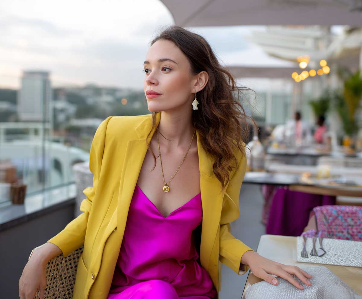 confident woman in a canary yellow blazer layered over a hot pink satin jumpsuit, rooftop restaurant setting, sunset sky, soft wind in hair, chic and vibrant style, natural makeup look
