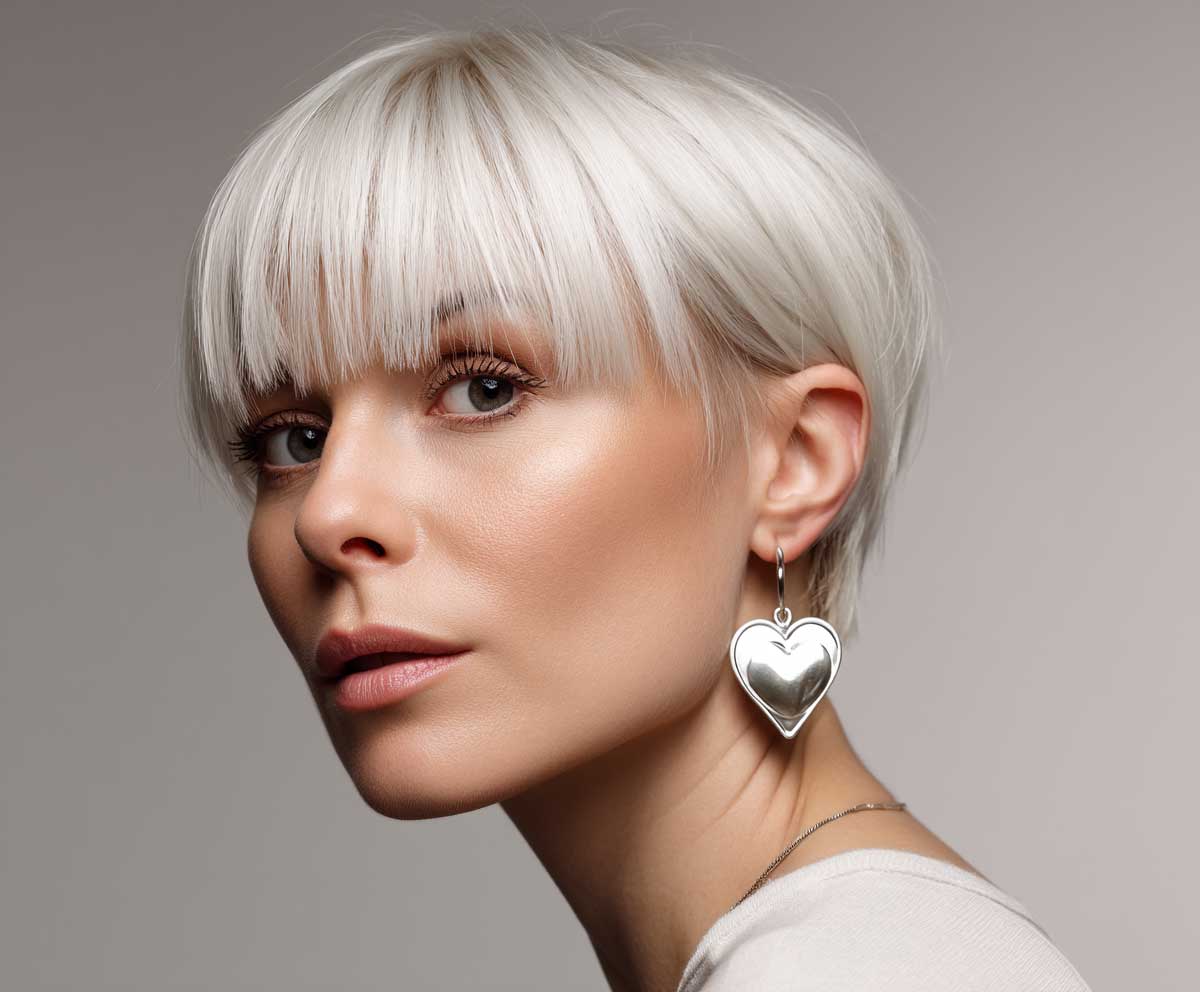 Trendy woman with a heart shaped face, pearl blonde short straight pixie haircut with micro fringe, close-up studio shot, clean backdrop, fashion-forward style