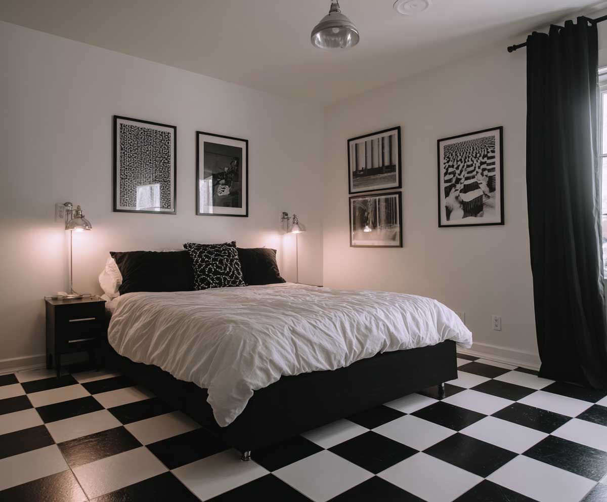 monochrome guest bedroom with black and white checkerboard floor, minimal furnishings, white walls, modern black bed frame, graphic art prints, bold contrast lighting, clean dramatic style