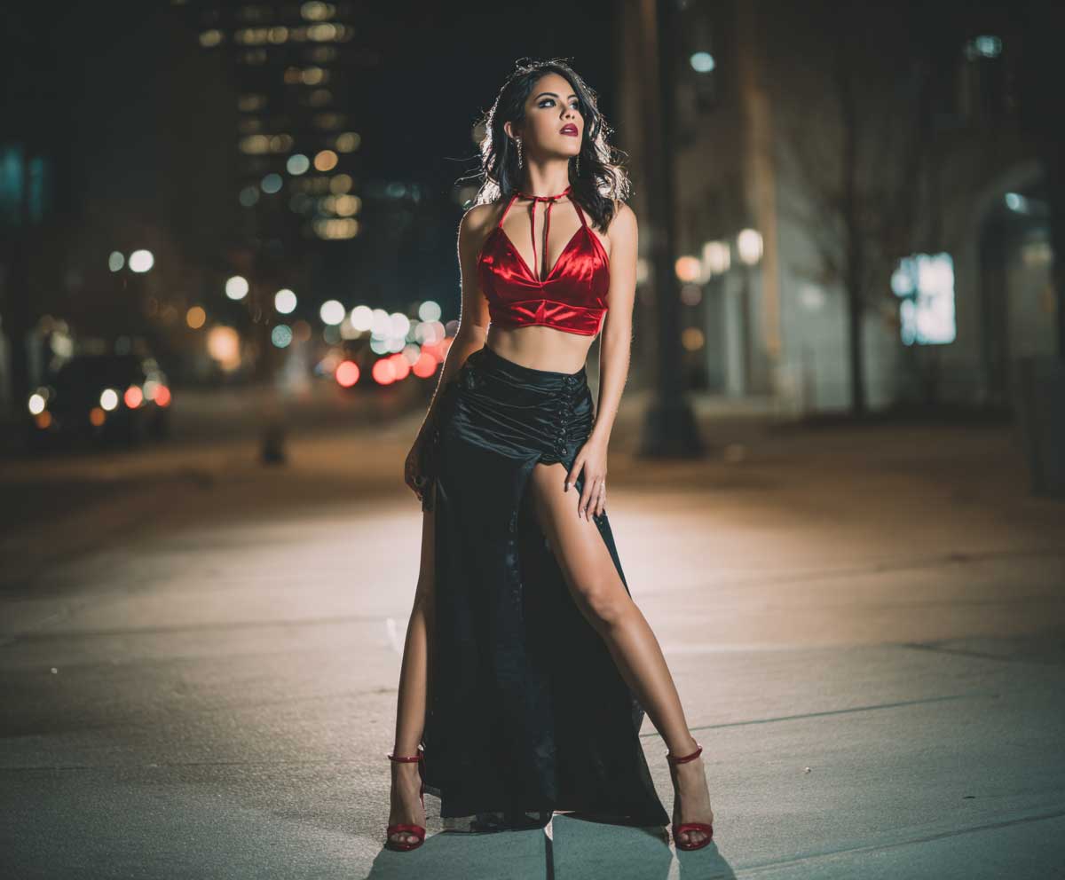 full-body shot of a confident woman wearing a red satin halter top and a sleek black skirt with a thigh-high slit, moody evening lighting, glossy heels, nighttime city street backdrop, soft shadows, minimal accessories