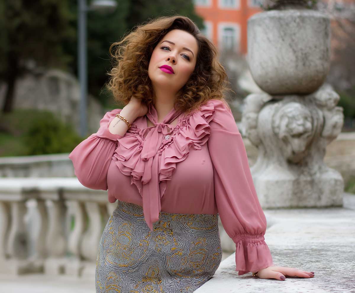 plus size woman in a patterned pencil skirt and pink ruffle blouse, posing in a city park, soft lighting, full-length feminine fashion look, spring style, cheerful mood