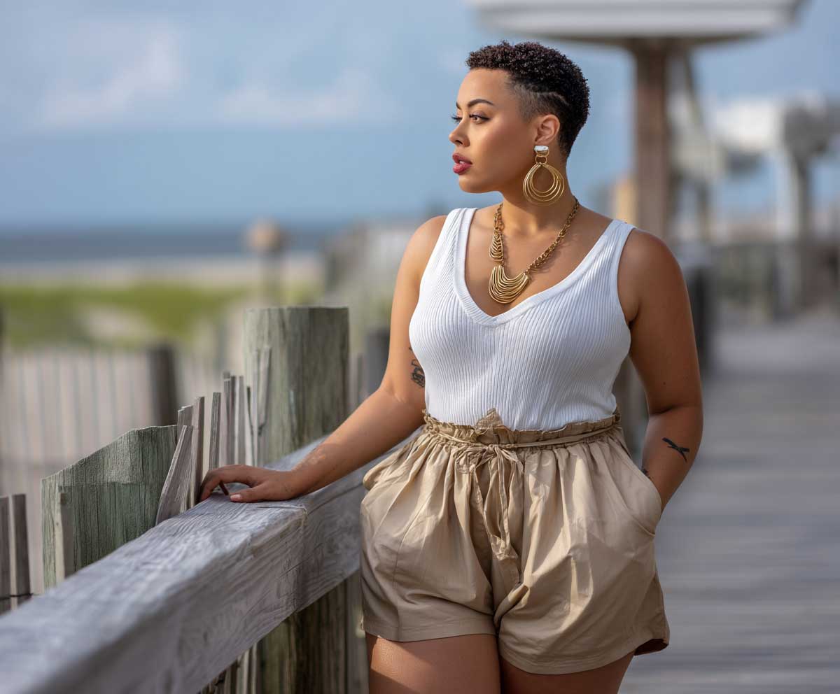 plus size woman in khaki paperbag shorts and a white ribbed tank top, standing near a coastal boardwalk, full body outfit, soft natural light, casual summer fashion, relaxed confident vibe