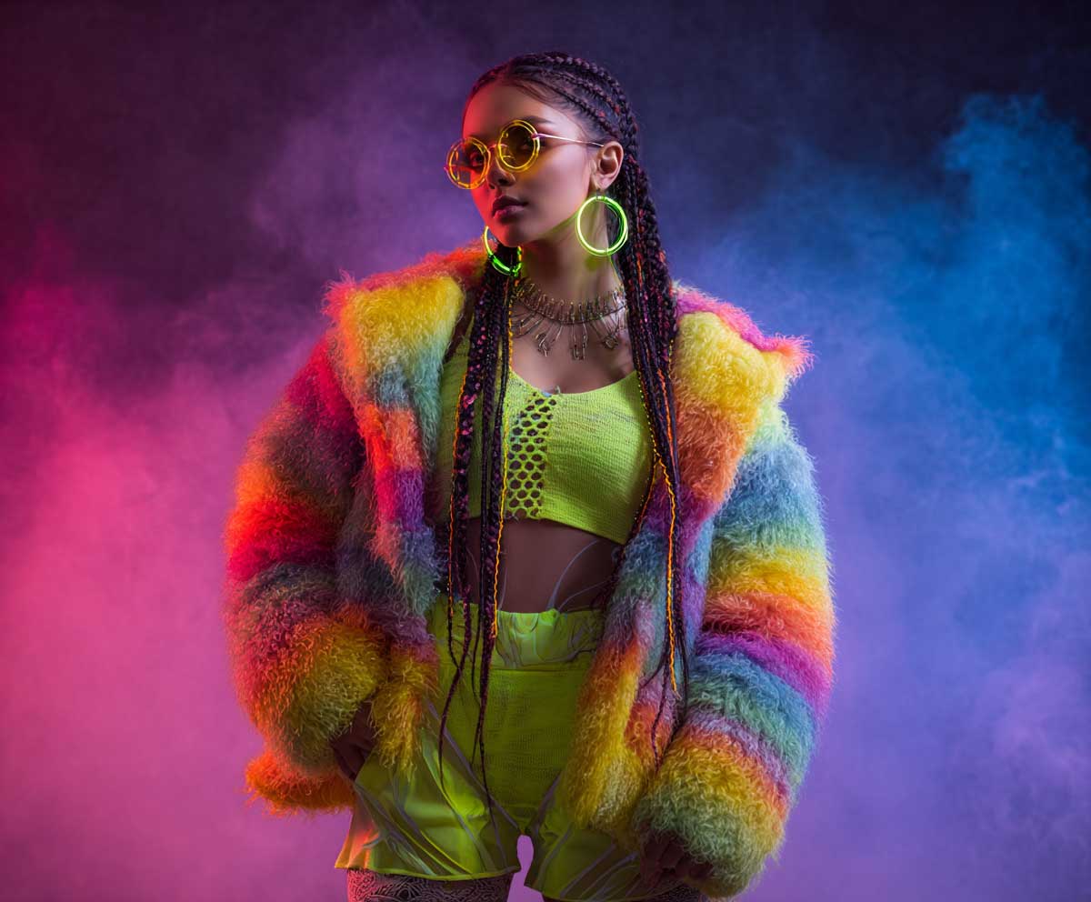 fashion photo of a model wearing an oversized rainbow furry coat and neon green bike shorts, LED earrings, braided hair with glow extensions, colorful rave background with smoke effects, standing confident pose, vibrant lighting