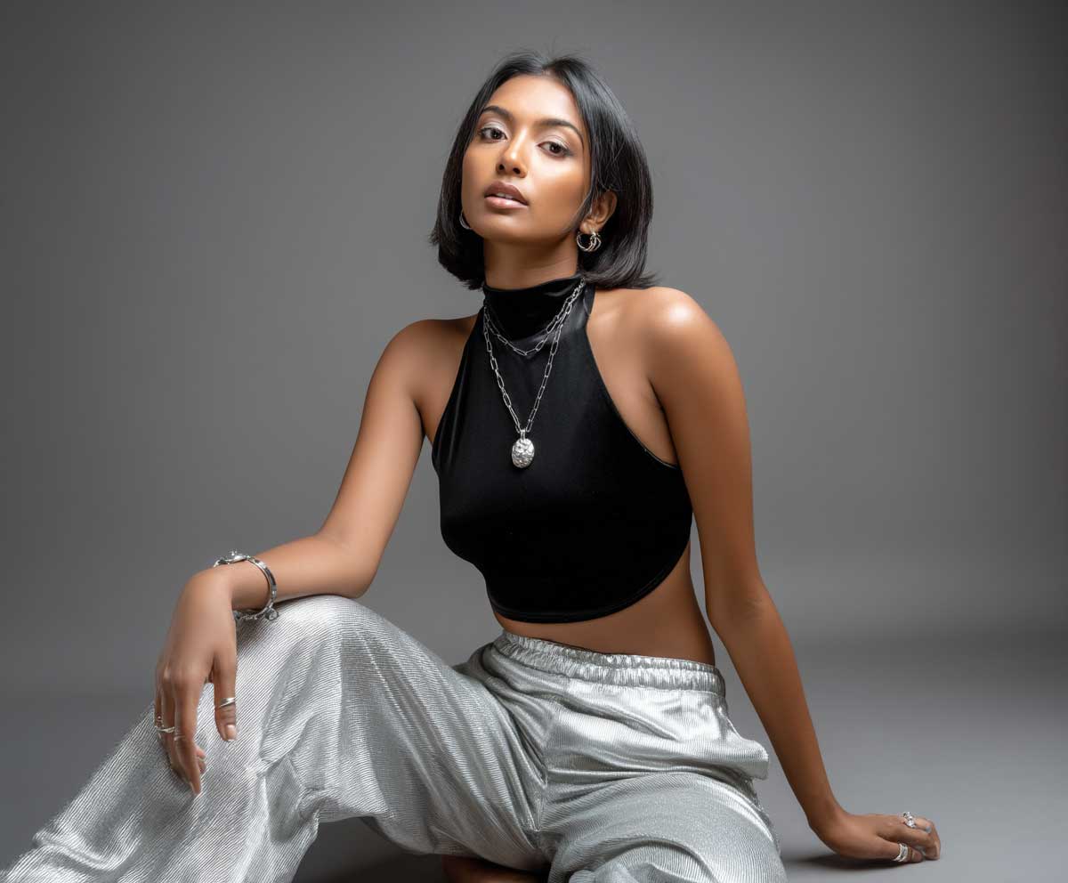 woman in black halter-style open back top and shiny silver trousers, soft indoor lighting, minimal modern background, confident full body pose, sleek hair, stylish accessories