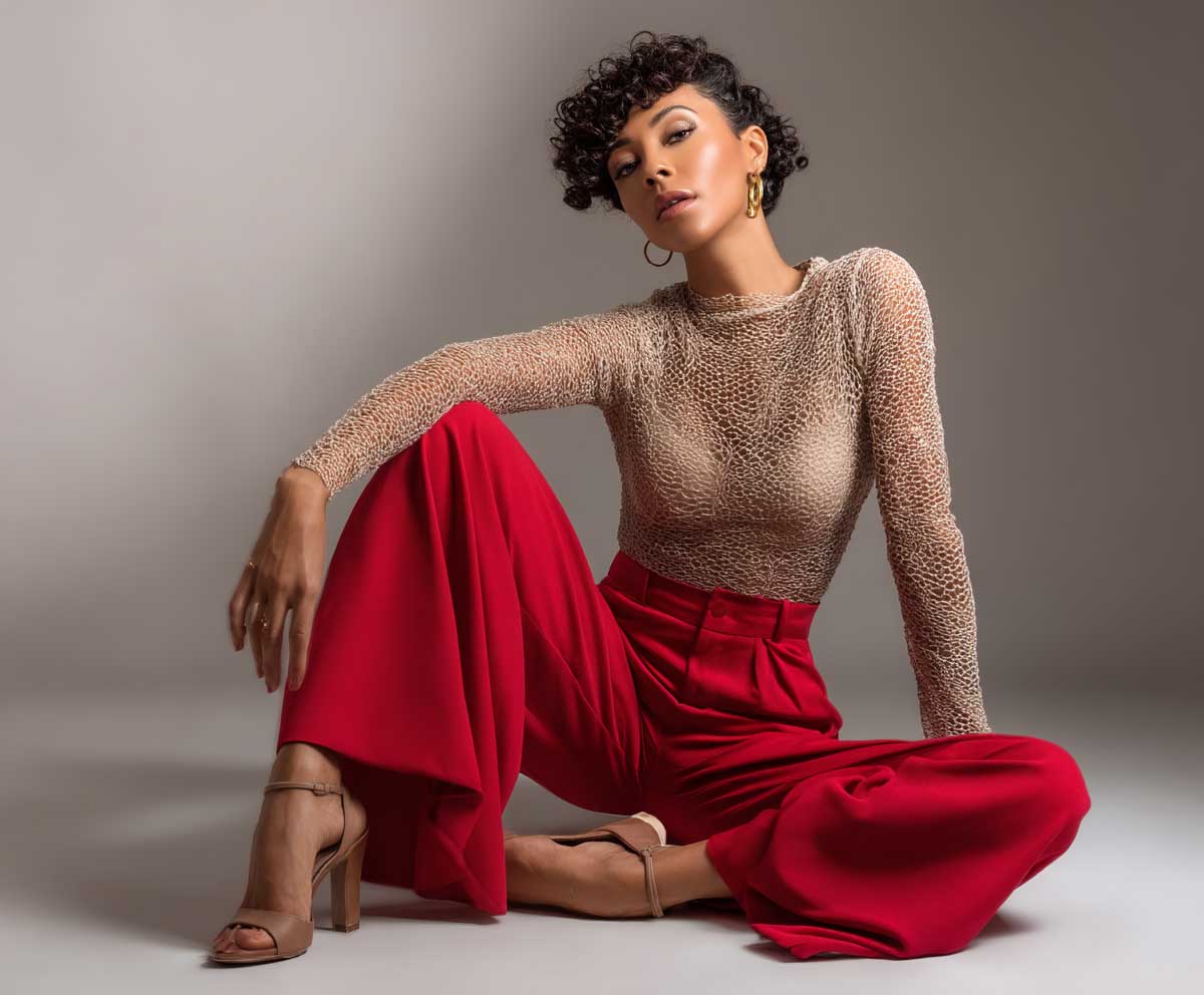 woman wearing soft beige mesh bodysuit and high waist red wide leg trousers, fashion studio setup, bold color styling, relaxed confident posture, warm lighting, full body look