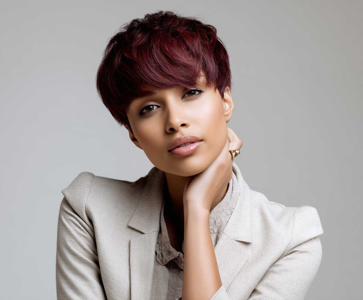 stylish woman with burgundy short pixie cut, soft face-framing bangs, business-casual outfit, light gray background, natural expression, elegant posture, fashion editorial tone