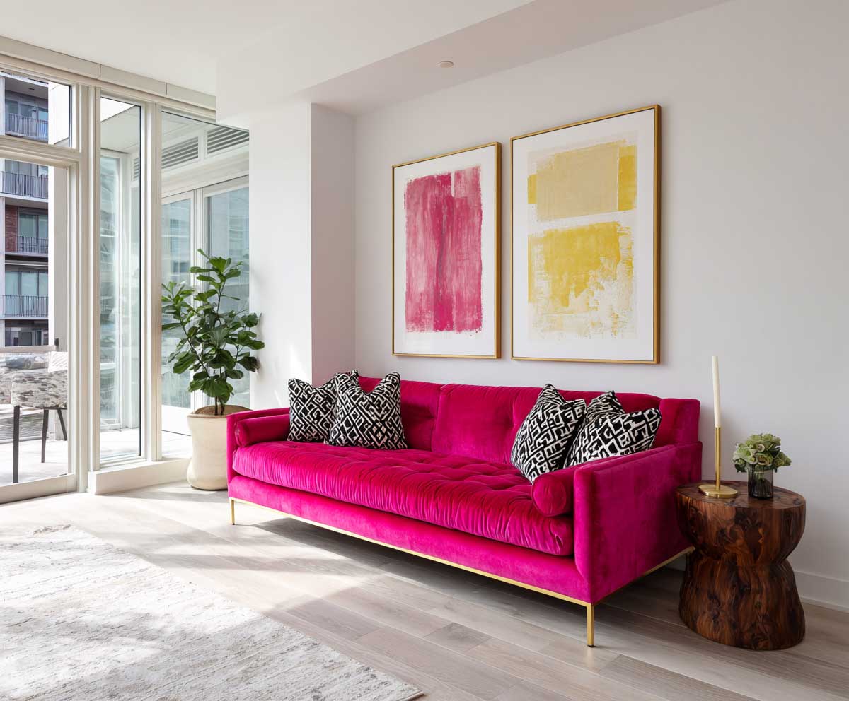 a stylish modern apartment living room with a bold hot pink velvet sofa, light wood flooring, white walls, geometric throw pillows, abstract wall art, floor-to-ceiling windows, minimal yet chic decor