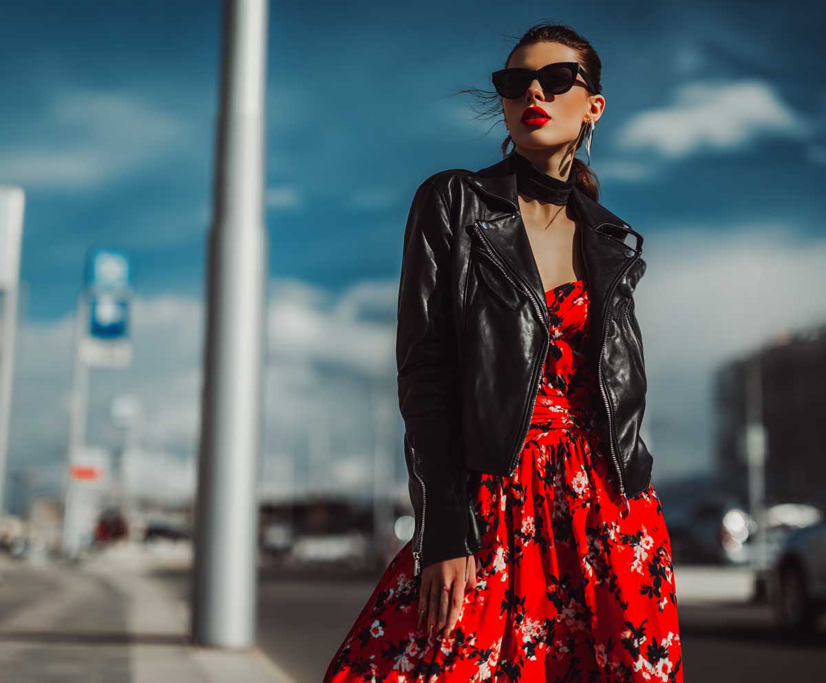 fashion-forward woman in brown leather jacket with dark floral maxi dress, ankle boots, autumn park scene, soft focus background, layered outfit look