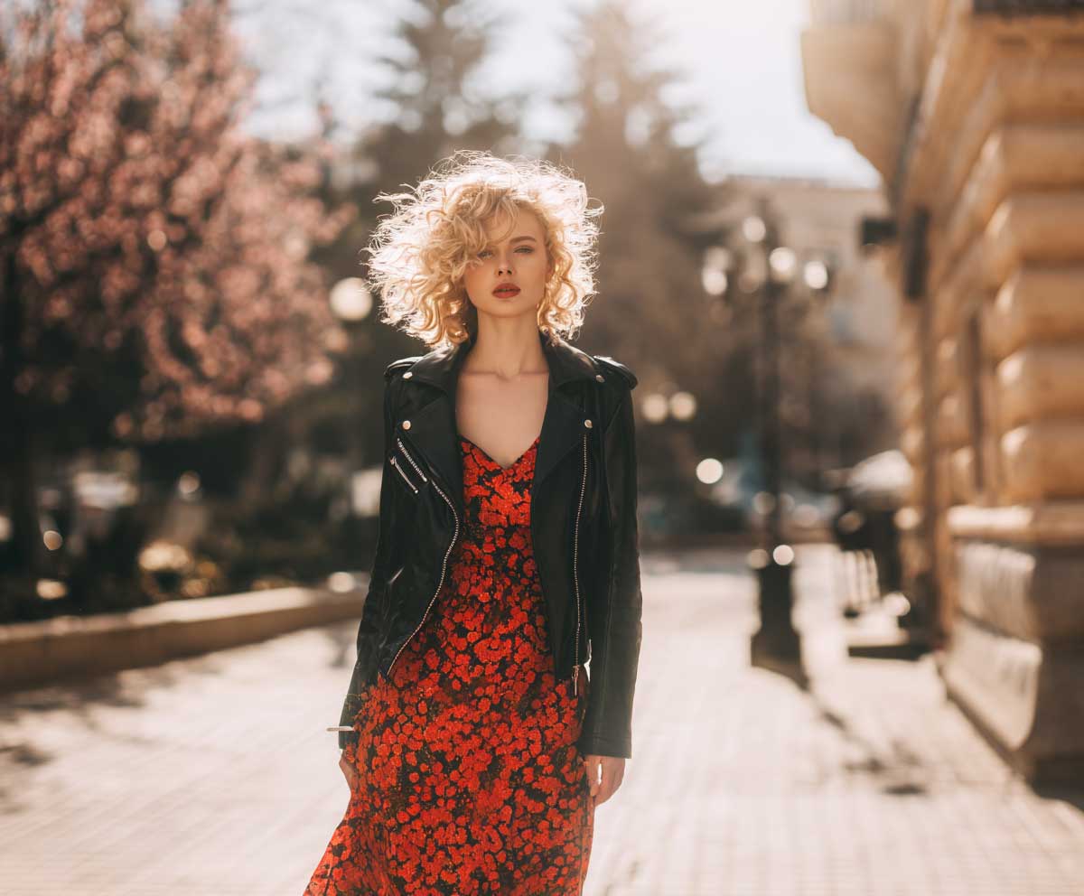 fashion-forward woman in brown leather jacket with dark floral maxi dress, ankle boots, autumn park scene, soft focus background, layered outfit look