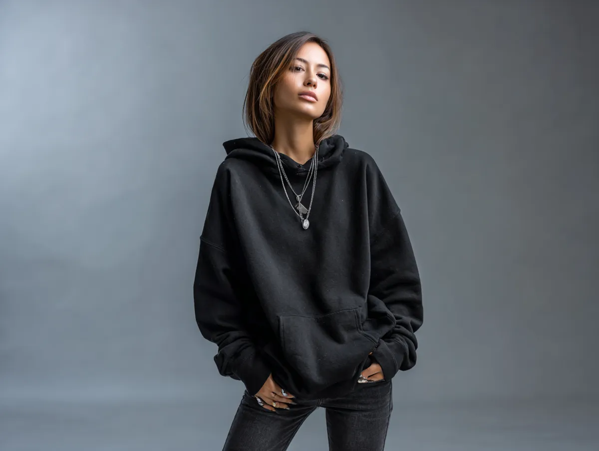 A young model in a standing pose wearing a black hoodie and skinny jeans, emo outfit ideas for a minimalist clothing catalog photo shoot, moody studio lighting, fashion editorial photography
