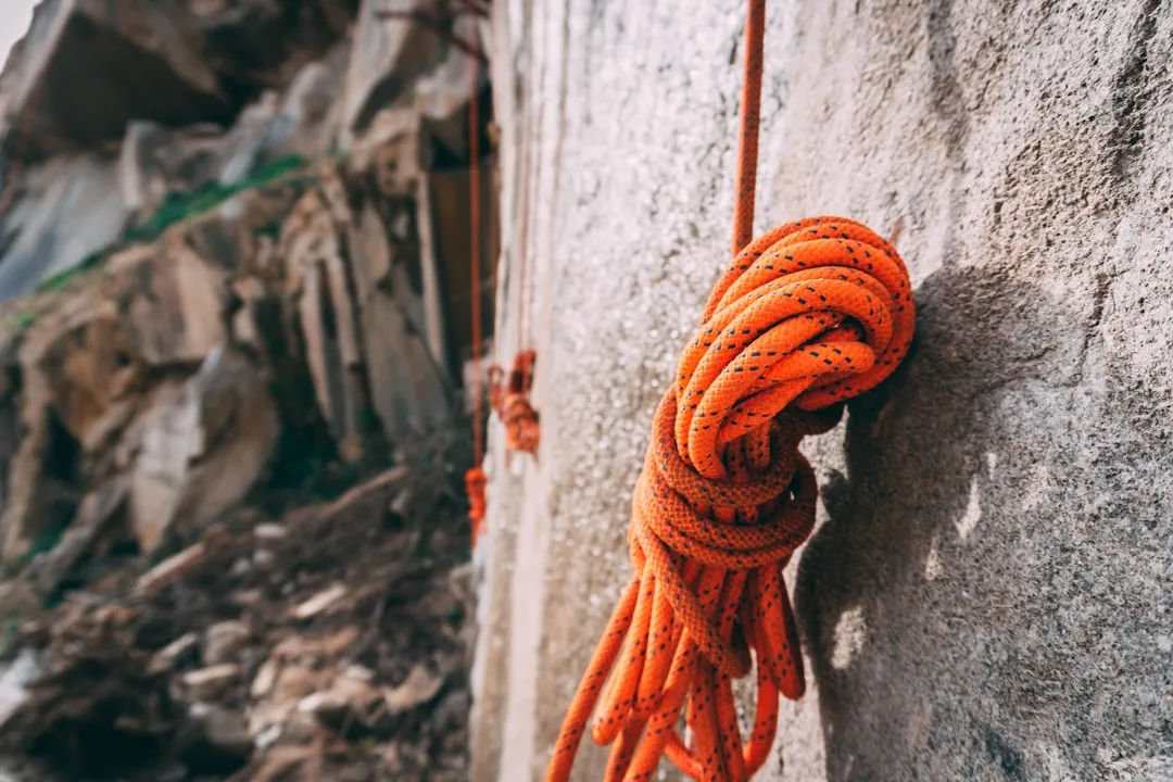 Adventurer securing climbing rope on mountain cliff with adventure travel insurance protection detail 4