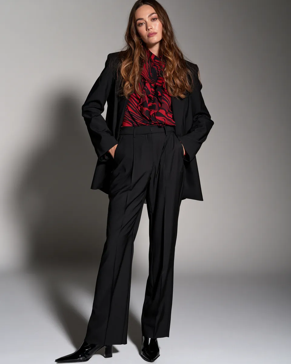 Studio fashion editorial featuring a woman in chic black pants and blazer combination, confident standing pose, high-fashion magazine aesthetic.