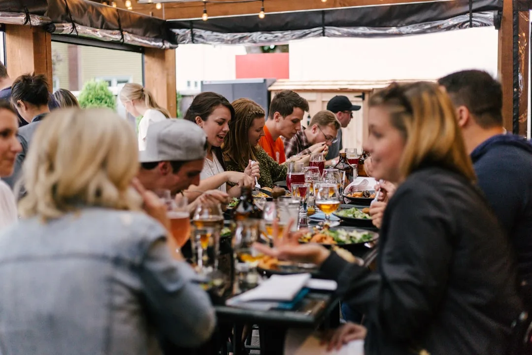 Eight people seated around small dining table sharing food and conversation