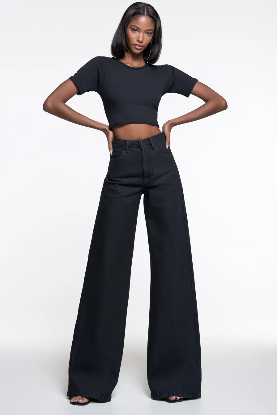 Woman in a stylish casual outfit with wide-leg jeans and a crop top on a white studio background