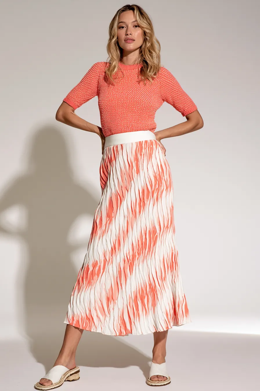 Female model in a chic casual outfit for women featuring a midi skirt and coral knit top in a studio setting