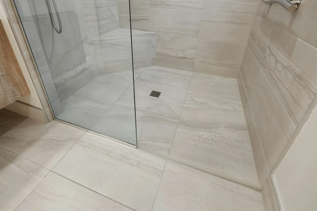 Close-up of cracked unsealed grout between bathroom floor tiles showing water discoloration