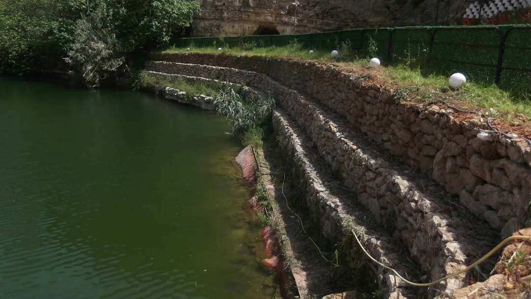 Residential gabion wall separating sloped yard with mixed stone fill and metal framework visible