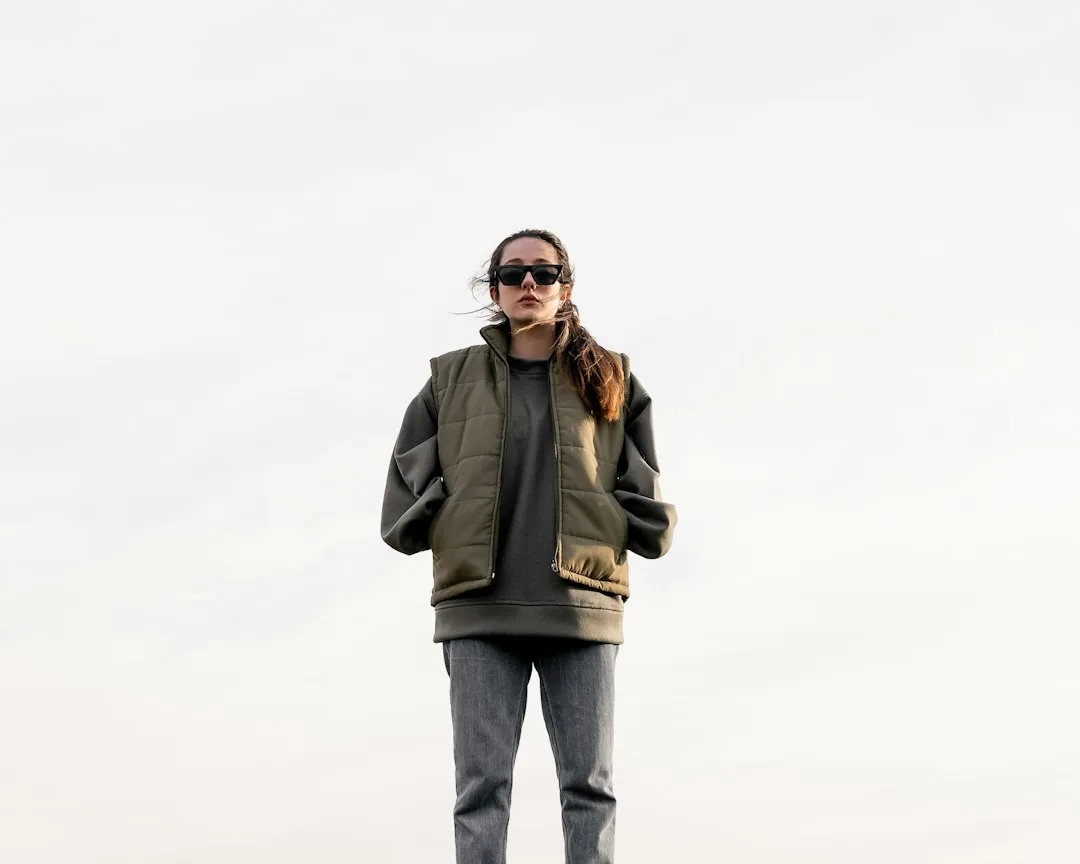 Woman wearing structured tan utility vest layered over white shirt with tailored trousers and minimalist sneakers