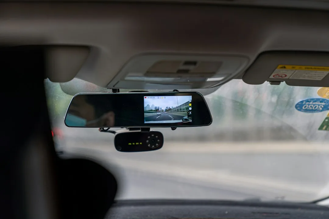 Close-up of a compact dash camera suction-mounted on a windshield near the rearview mirror