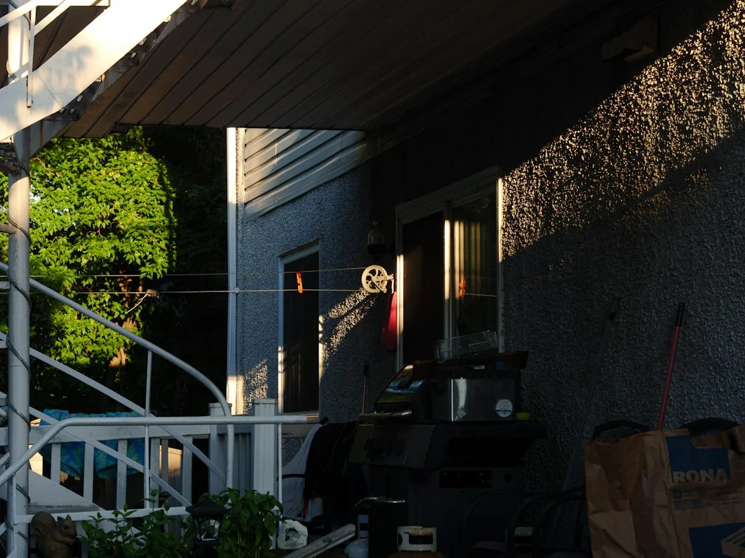 Shade sail installation anchored to house wall and wooden posts in modern landscape